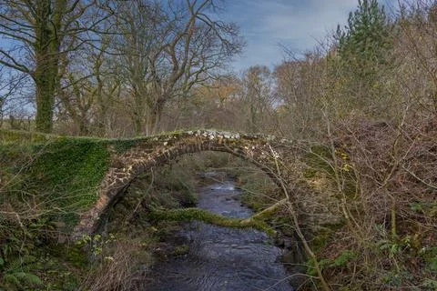 Ancient stone bridge arches over clear, flowing stream Stock Photos