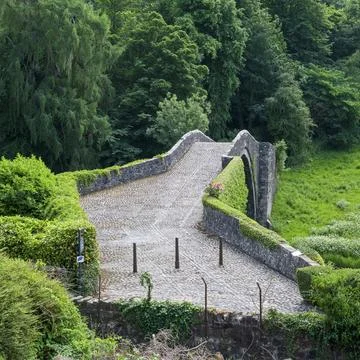 Ancient stone bridge curves through lush greenery Stock Photos