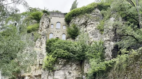 Ancient stone cliff face embedded with a historic building, lush greenery. Video stock 345413982