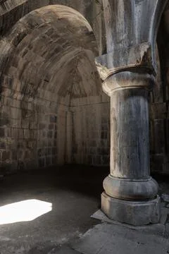 Ancient stone column and vaulted arch inside a dim medieval chapel. Haghpat.. Stock Photos