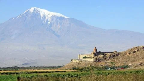 Ancient stone monastery sits atop a rocky hill beneath a towering snow-capped Stock Photos