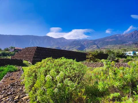 Ancient stone structures stand in the sunlight with mountains and blue sky .. Stock Photos