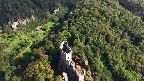 Ancient stone tower ruin rises through emerald forest canopy above rugged c.. Stock Photos