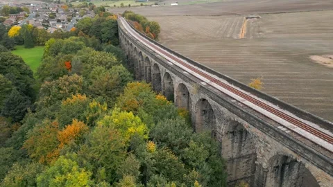 Ancient stone viaduct curves through autumnal trees Stockbeeldmateriaal 343872269