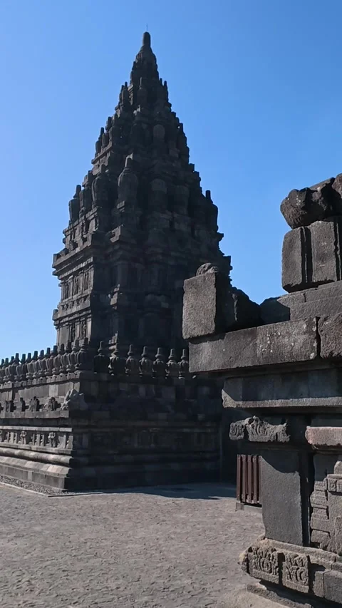 Ancient stone walkway passes a shadowed Prambanan Temple tower and open cou.. Stock Footage 341543412