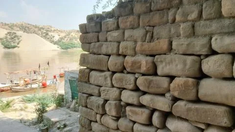 Ancient Stone Wall Overlooking Muddy River And Traditional Wooden Boats Foto stock