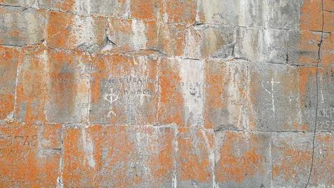 Ancient stone wall texture with orange lichen and old graffiti  Stock Photos
