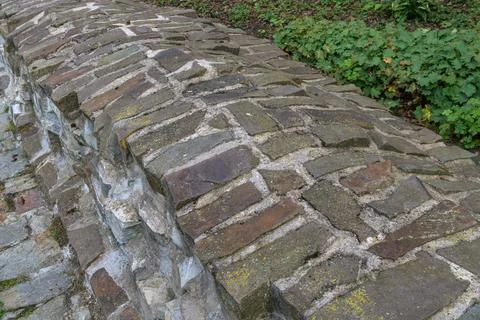 Ancient stone wall with unique patterns in a lush green park area Stock Photos