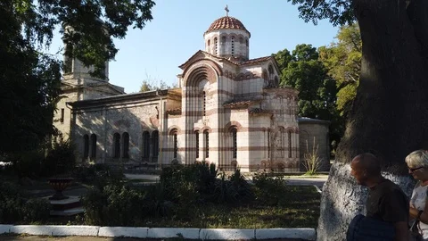 An ancient temple stands in the thick of trees. A man and a woman pass by. Vídeos de archivo 115788824