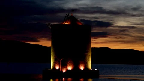 An ancient windmill with romantic lights on the sea bay at sunset Pan view Stock Footage 104516720
