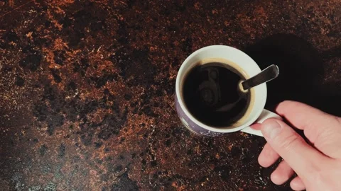 And picking up a cup of black coffee from a dark textured table top Stock Footage 334885015