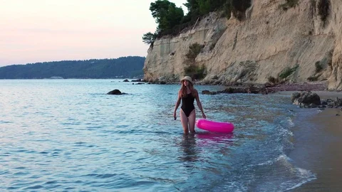 And stone cliff hanging over calm blue sea waves as fit young girl walks with Stock-Footage 97127628
