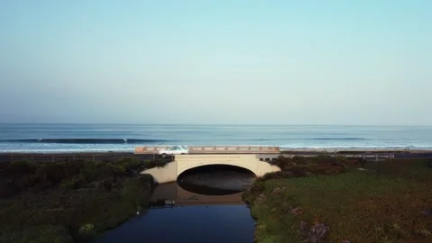 UP AND UNDER BRIDGE - REVEAL - OCEAN - WAVES - SURF Stock Footage
