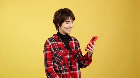 Androgynous person smiling while sending a message with a mobile 스톡 동영상 234866136