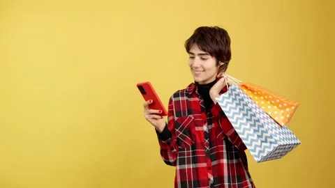 Androgynous person using a mobile while holding shopping bags Vídeo Stock 239215834