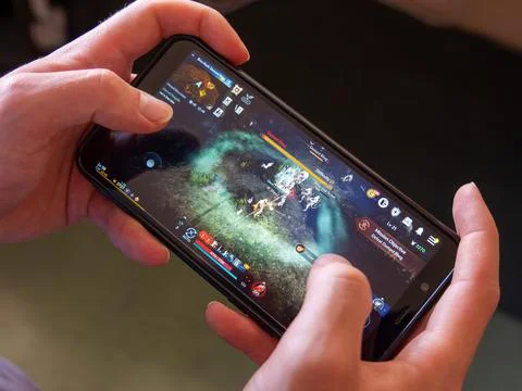 A android phone in the hands of a white man. Playing mobile MMORPG Black Desert Stock Photos