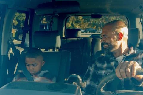 Angle from front window of car of father driving with son occupied with video Stock Photos