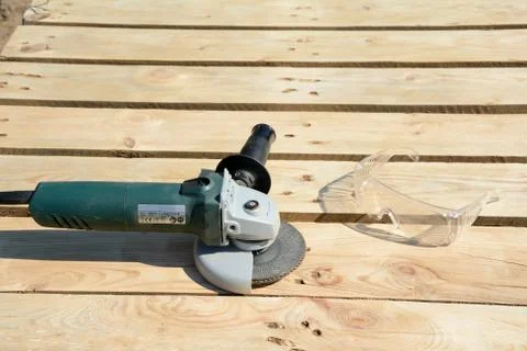 Angle grinder with abrasive disc and protective glasses on planks after work. Stock Photos