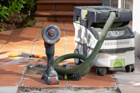 Angle grinder and construction vacuum cleaner are prepared for tile removal a Stock Photos