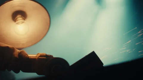 Angle grinder cutting steel beneath swinging workshop lamp glow Stock Footage 331697217