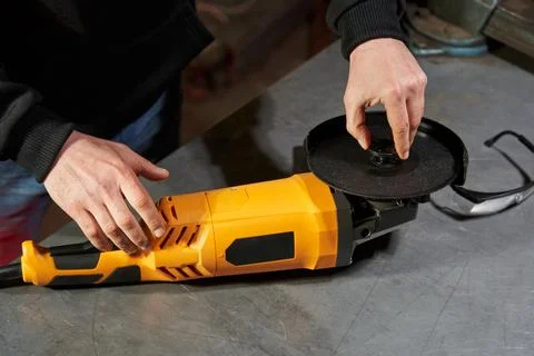 Angle grinder lies on an iron workbench. caucasian worker's hands install a Stock Photos