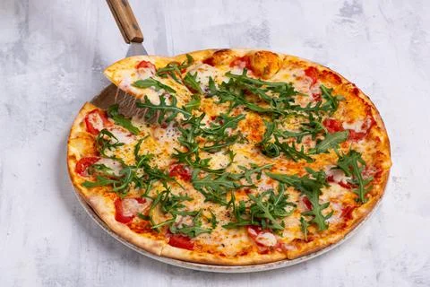 Angle shot of a spatula taking one piece of an arugula pizza. Stock Photos