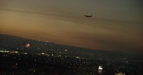 Angled aerial shot of plane flying above fireworks over city, sunset Stock Footage 101995110