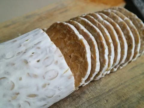 Angled close-up of sliced raw tempeh on a wooden board Stock Photos