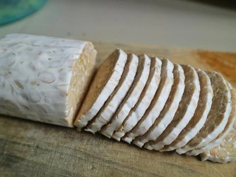 Angled close-up of sliced raw tempeh on a wooden board Stock Photos
