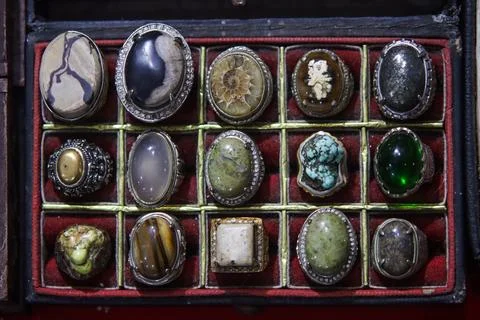 Angled macro shot of iridescent gemstone and dark agate rings in tray Foto stock