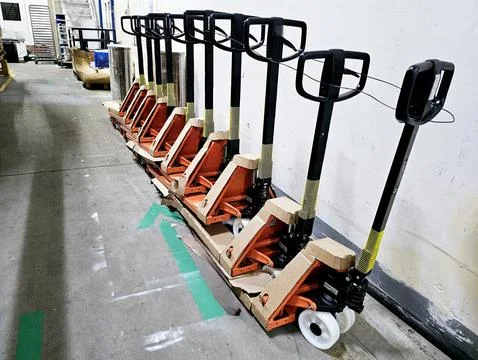 An angled, medium shot captures a row of new, black and orange pallet jacks . Stock Photos