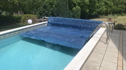 Angled perspective view of half removed blue solar pool cover with clean swimmin Stock Photos