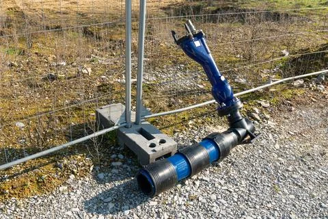 An angled plastic connecting pipe lying next to a metal fence. Stock Photos