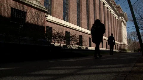 Angled shot with dramatic lighting of people passing in front of a classic brick Stock Footage 77378914