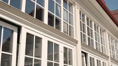 Angled view of a building facade with multiple white-framed windows, a clear sky Stock Footage 263029921