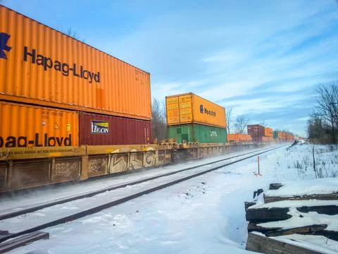 Angled view of orange, red and green rail cars travelling on train track. Stock Photos