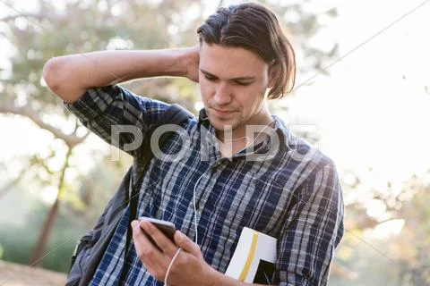 Angled View Of Young Man, Hand To Head, Looking Down At Smartphone