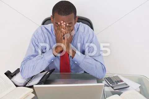 Angry Afro businessman with hands on face at desk Stock-Fotos