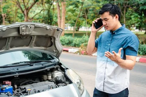 Angry Asian man and using mobile phone calling for assistance after a car bre Foto stock