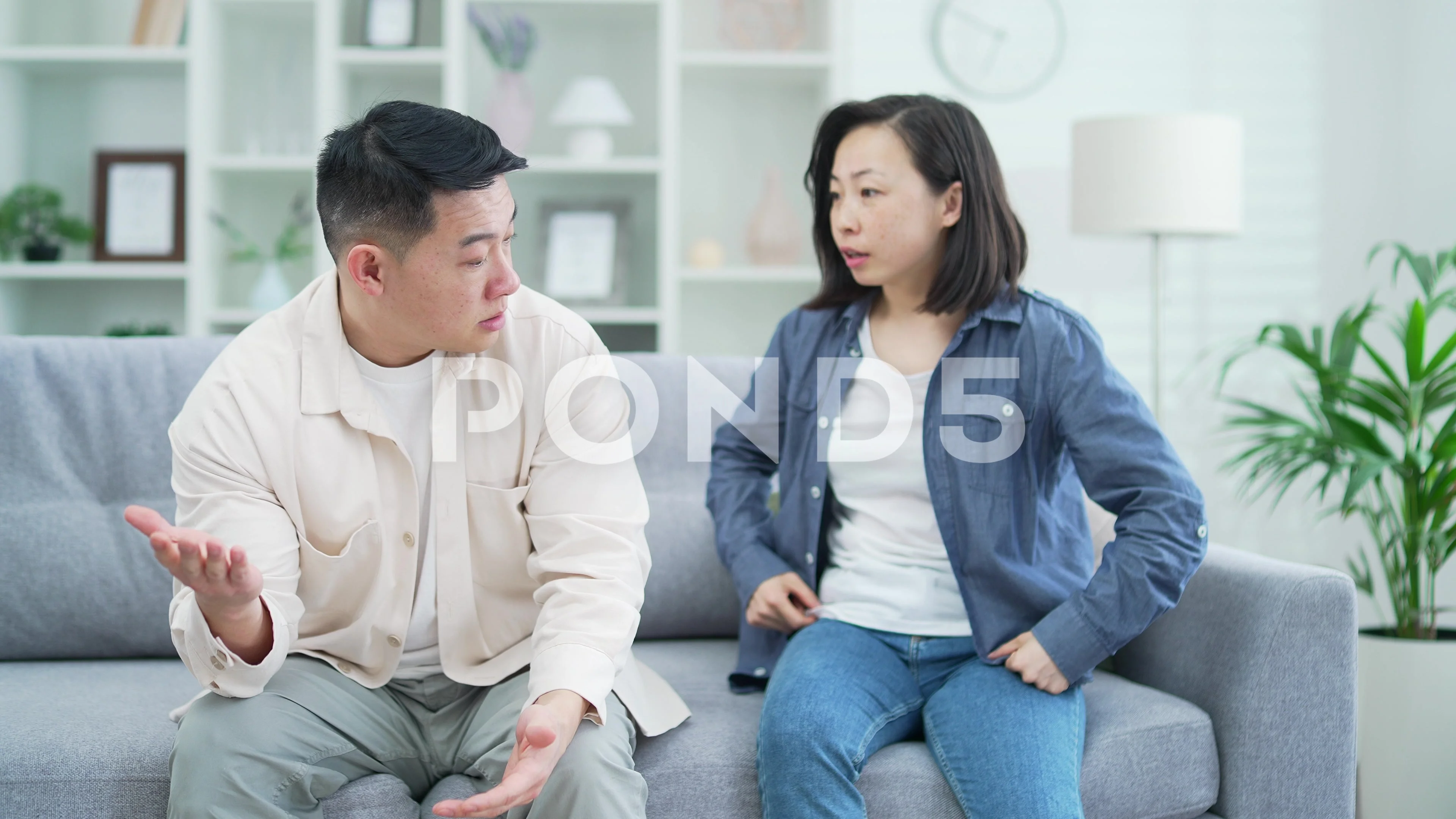 Angry asian wife arguing with husband sitting on sofa in living room at  home.