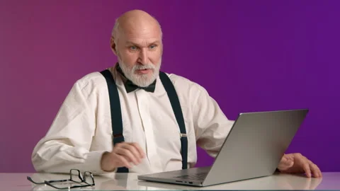 Angry Bald Man with Beard in White Shirt at Laptop on Pink-Purple Background Stock Footage 260541406
