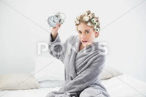 Angry blonde woman in hair curlers throwing her alarm clock Stock Photos