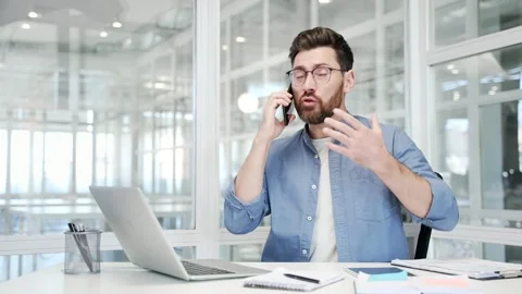 Angry businessman arguing talking on mobile phone sitting at workplace in office Stock Footage 305698598
