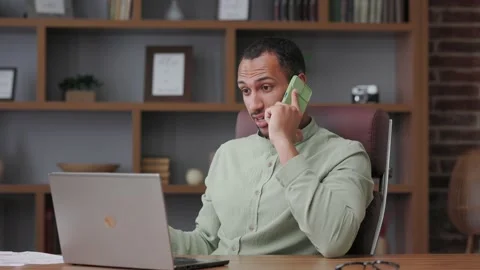 Angry businessman talking on the phone using laptop in office interior. Male Stock Footage 201973823