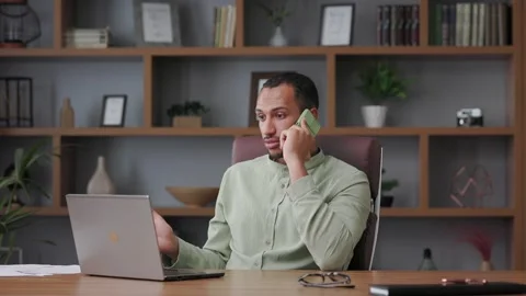 Angry businessman talking on the phone using laptop in office interior. Male Stock Footage 244646304