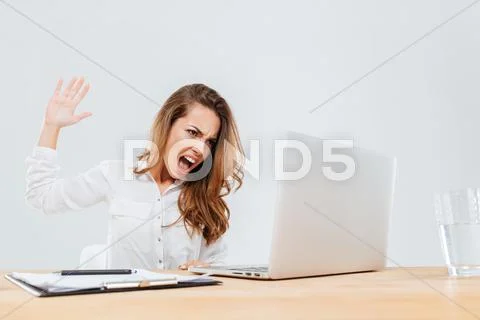 Angry businesswoman sitting and screaming at laptop in office Stock Photos
