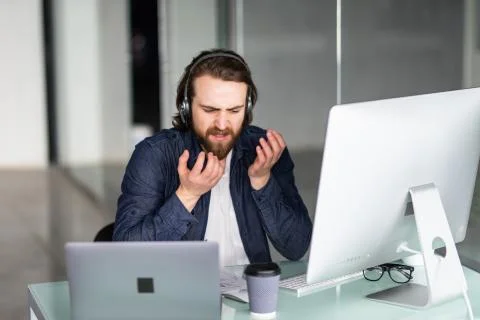 Angry call center operator working at his desk on computer and laptop Stock Photos