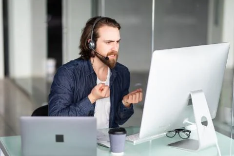 Angry call center operator working at his desk on computer and laptop Stock Photos
