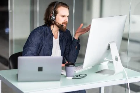 Angry call center operator working at his desk on computer and laptop Stock Photos