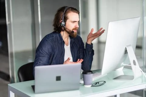 Angry call center operator working at his desk on computer and laptop Stock Photos